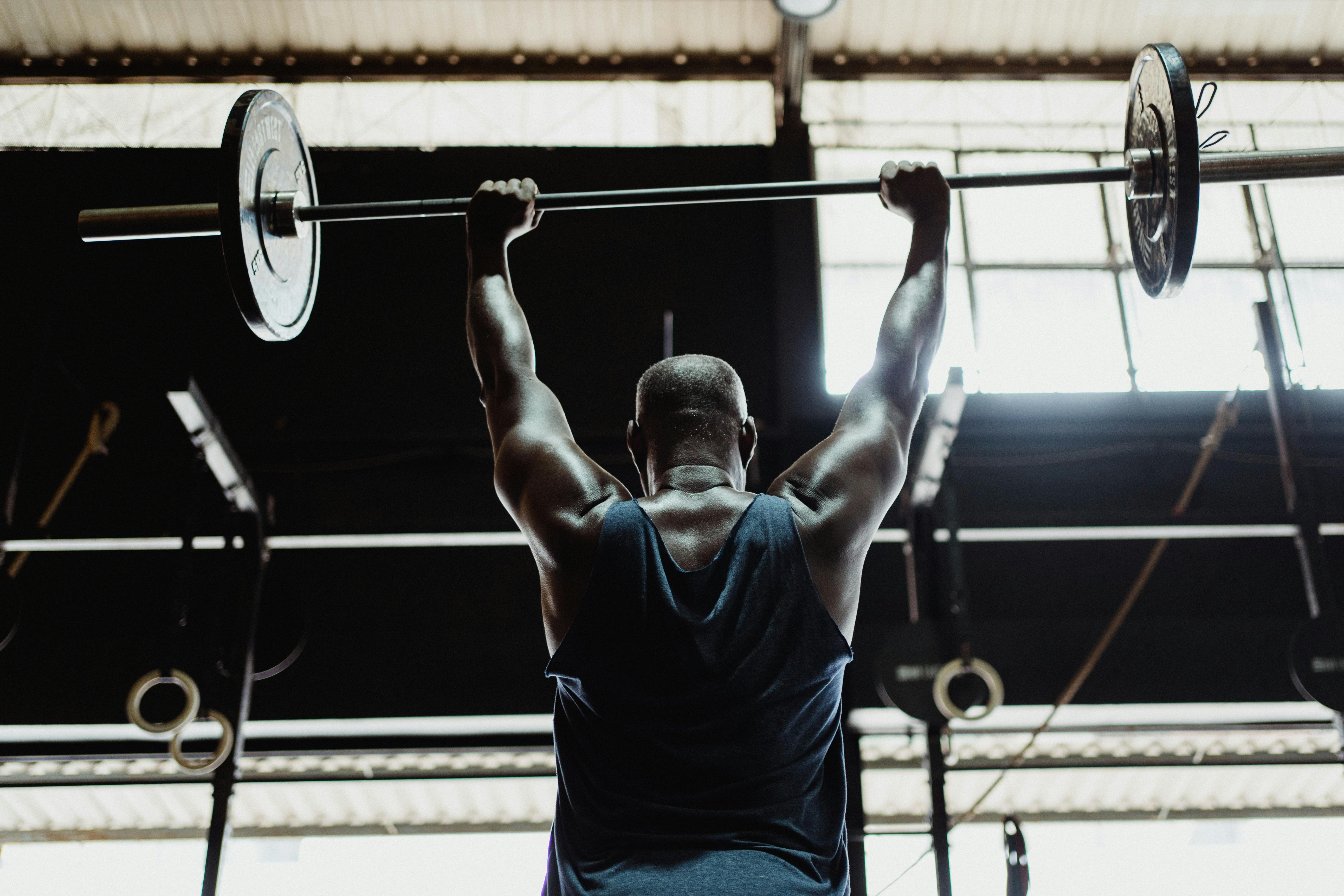 Rear view of lifter performing barbell shoulder press overhead in a gym setting