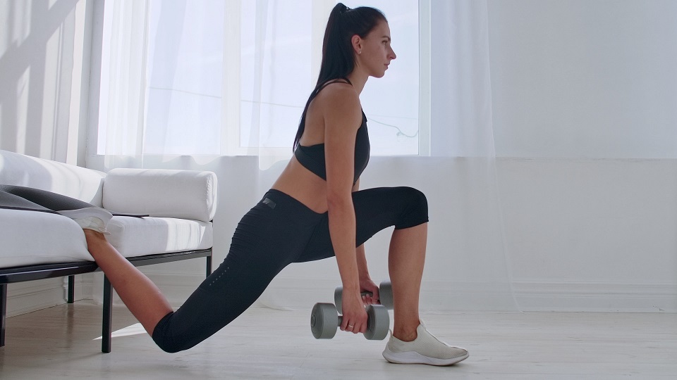 Lifter performing Bulgarian split squat with rear foot elevated on a bench in a gym